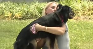 Frau umarmt großen schwarzen Hund im Freien.