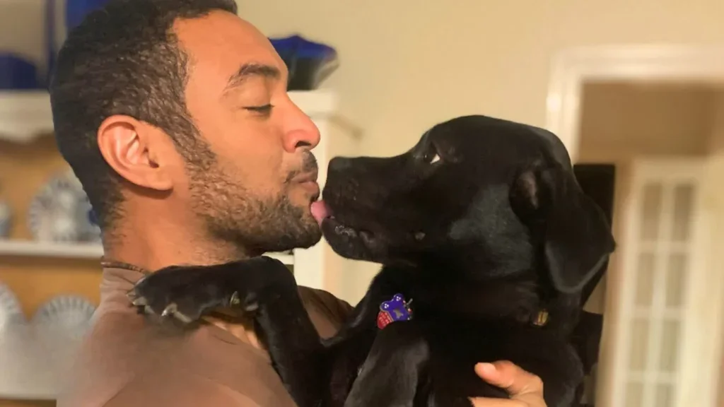 Mann kuschelt mit schwarzem Labrador.