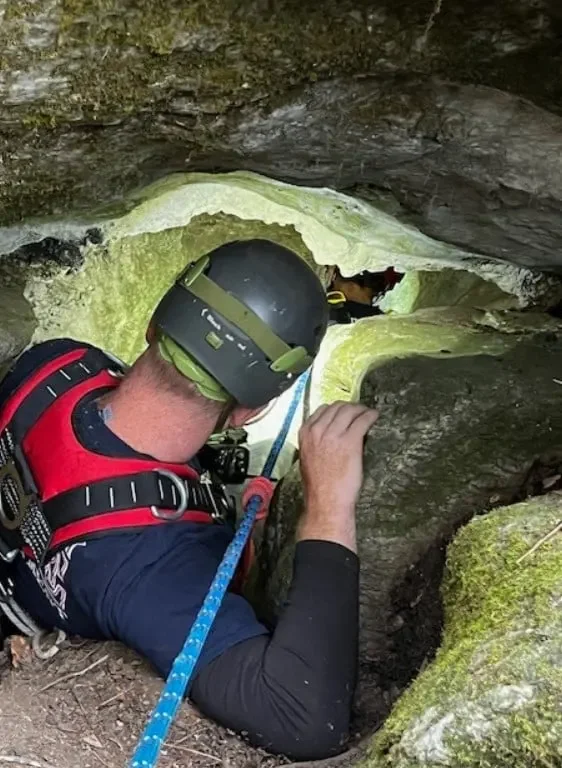 Person kriecht durch enge Höhlenöffnung.