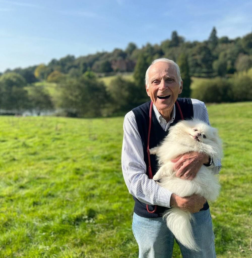 Älterer Mann hält lachend einen weißen Hund.